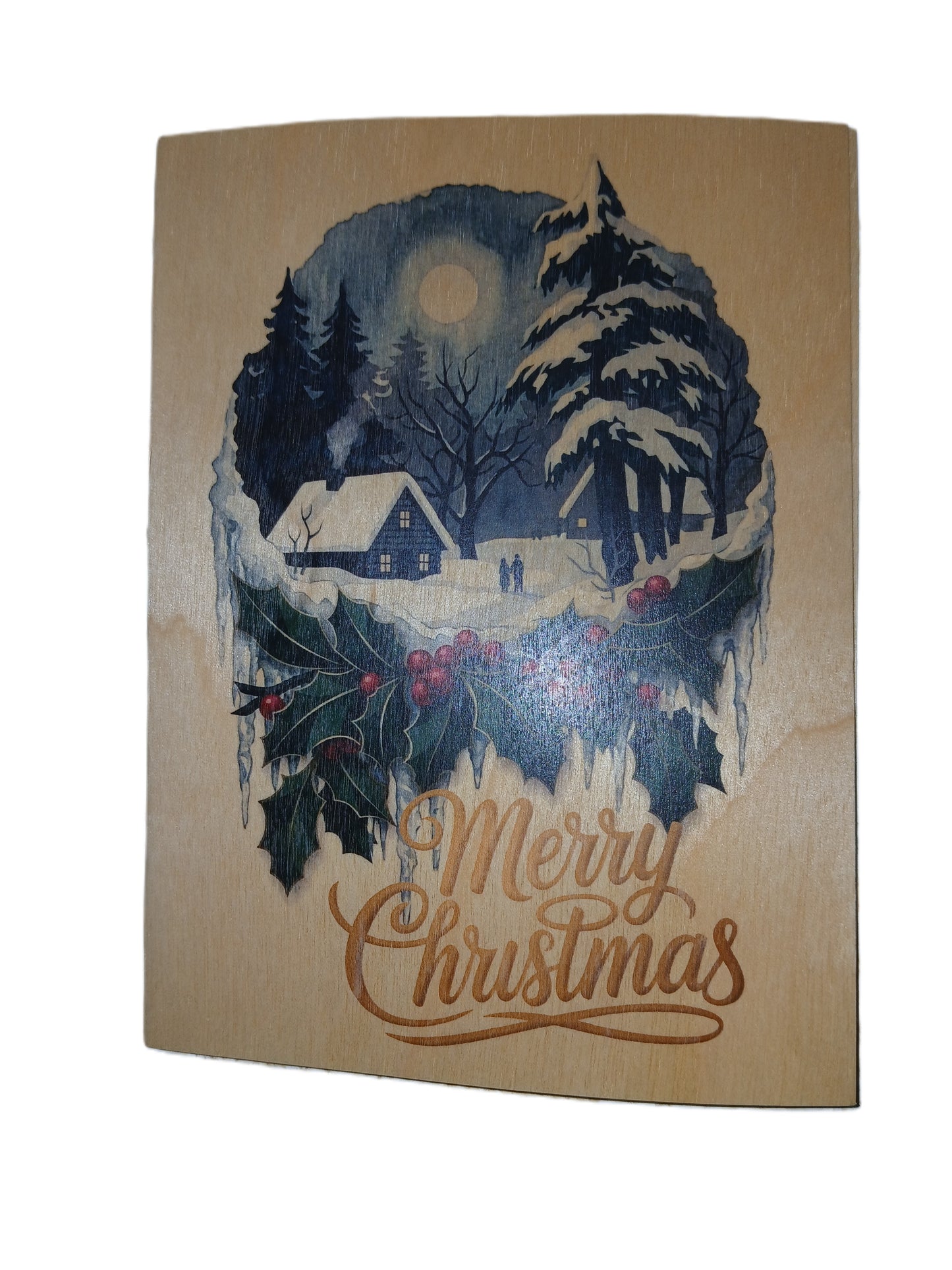 A rectangular wooden Christmas card featuring a winter scene with snow-covered trees, a small cabin, a full moon, holly, and the words 'Merry Christmas' in brown script on a light wood background.